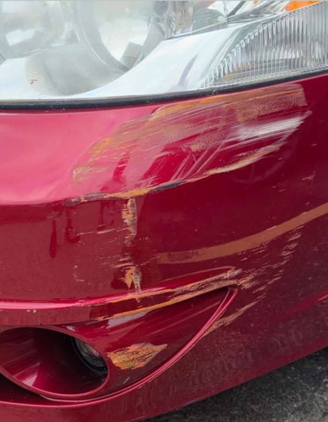 Deep scuff and paint transfer across the corner of a red bumper before correction