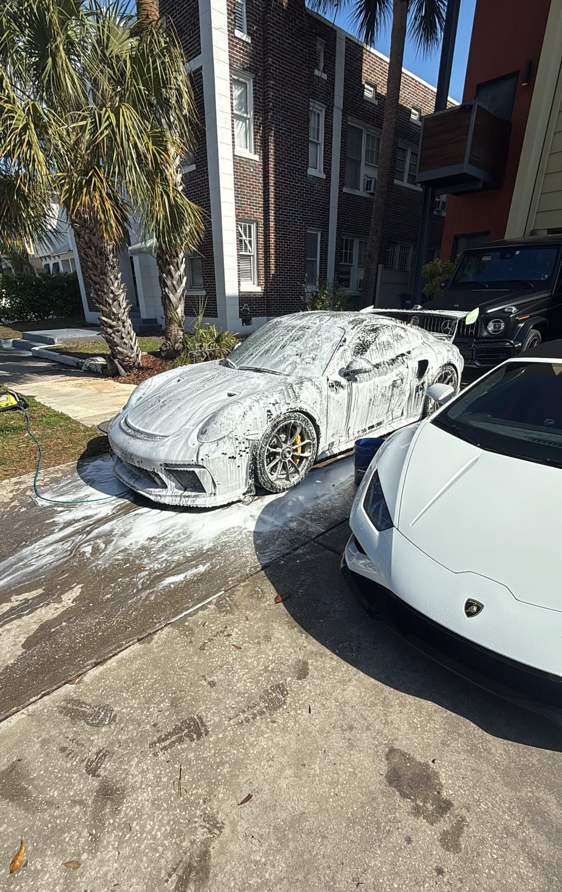 A coated sports car under a full blanket of snow foam during a maintenance wash